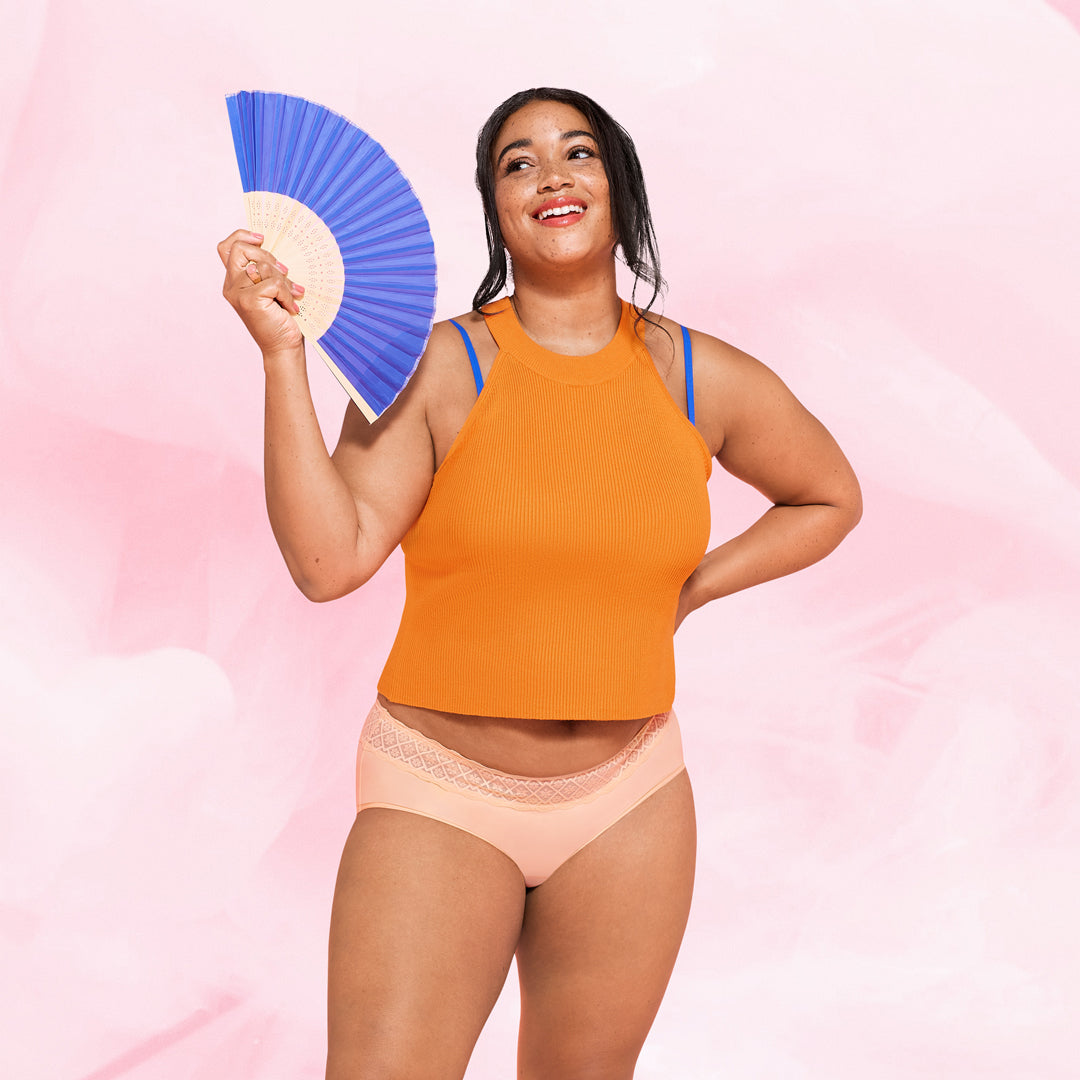 Femme en robe orange tenant un éventail, portant la culotte menstruelle Hipster Full Lace Moderate, confortable et ultra-absorbante, idéale pour un flux modéré.