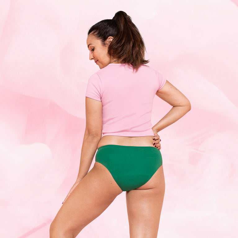 Femme portant la culotte menstruelle ComfortFit Essentielle Brazilian Heavy, taille haute, offrant protection discrète et durable jusqu'à 12 heures, ajustée à la taille de pantalon.