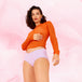 Femme portant un ComfortFit Essentielle Hipster Moderate, posant en sous-vêtement blanc avec un pull orange, illustrant le confort et la coupe ajustée pour règles.