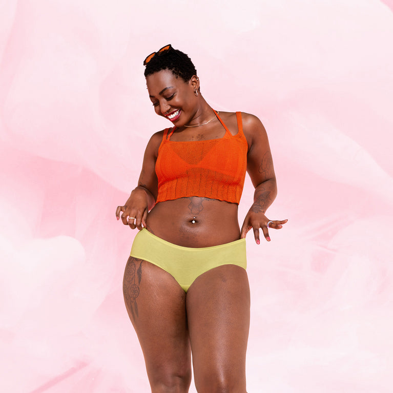 Femme souriante portant le ComfortFit Essentielle Hipster Heavy, un sous-vêtement menstruel confortable et réutilisable, offrant une protection discrète et fiable.