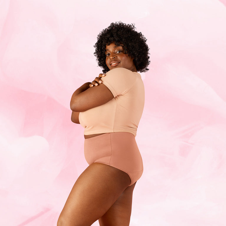 Femme en culotte menstruelle Confort Premium High Waist Moderate, bras croisés, souriante, illustrant confort et élégance de la taille haute pour flux modéré.