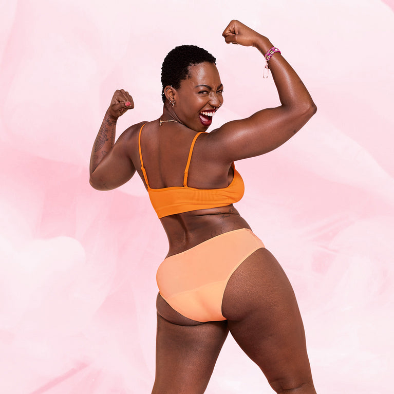 Femme portant la culotte menstruelle Brazilian Moderate, flexion des muscles, illustrant confort et élégance avec protection maximale pour flux modéré, technologie TriTech Performance.