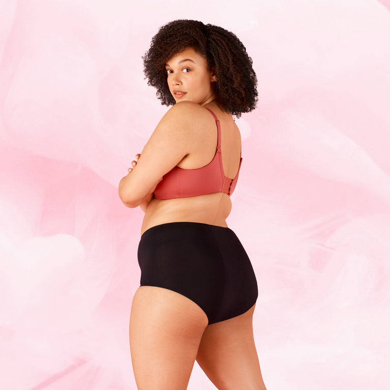 Une femme portant la culotte menstruelle Nuit High Waist Nana® ComfortFit, coupe taille haute, bras croisés, pour protection nocturne jusqu'à 12 heures.