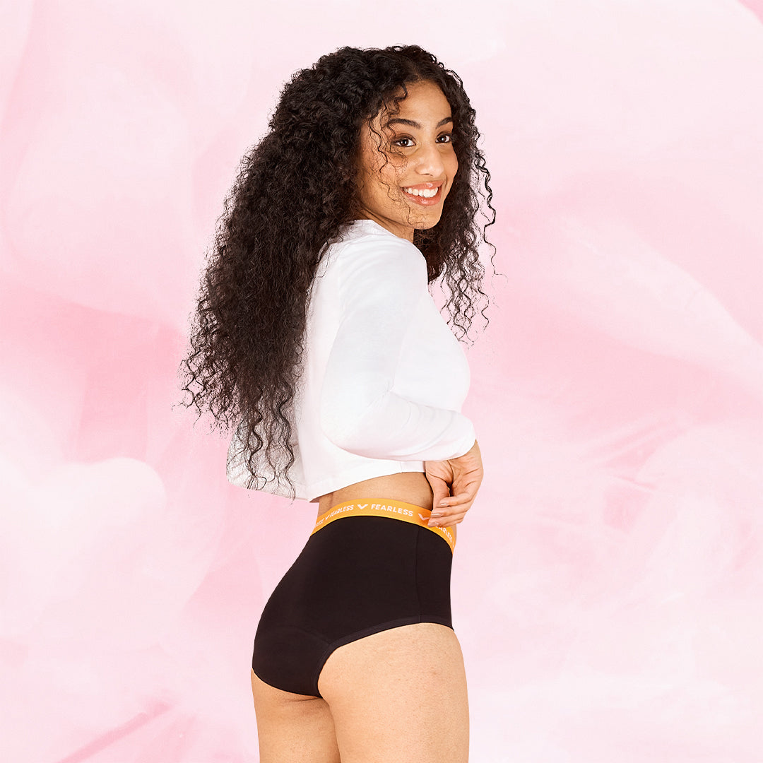 Femme souriante portant les culottes menstruelles Ados - Brief Logo Waistband Moderate, avec taille haute et ceinture motifs « Fearless », conçues pour confort et protection.